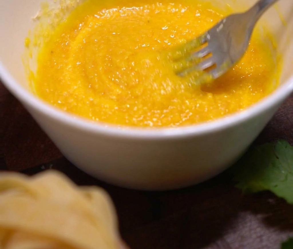 Eigelb und Parmesan werden in einer weißen Schüssel mit einer Metallgabel vermischt.
