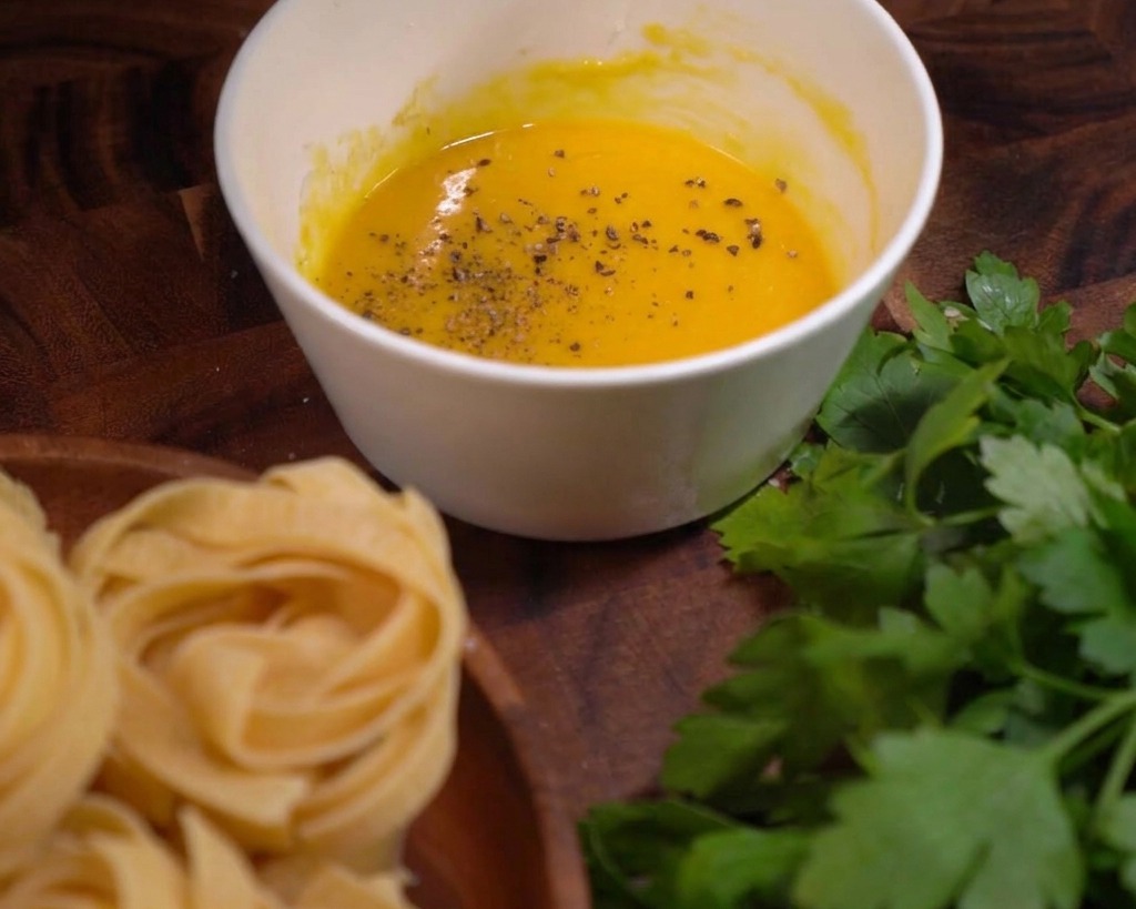 Grob gemahlene schwarze Pfefferkörner auf der glatten, gelben Ei-Käse-Sauce.
