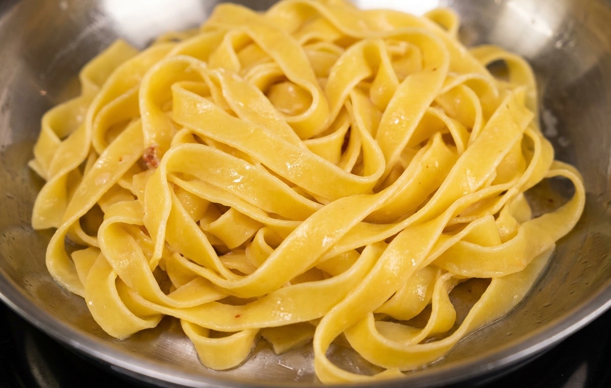Fettuccine-Nudeln werden in eine Pfanne mit goldbraunem Speck und Fett gegeben.
