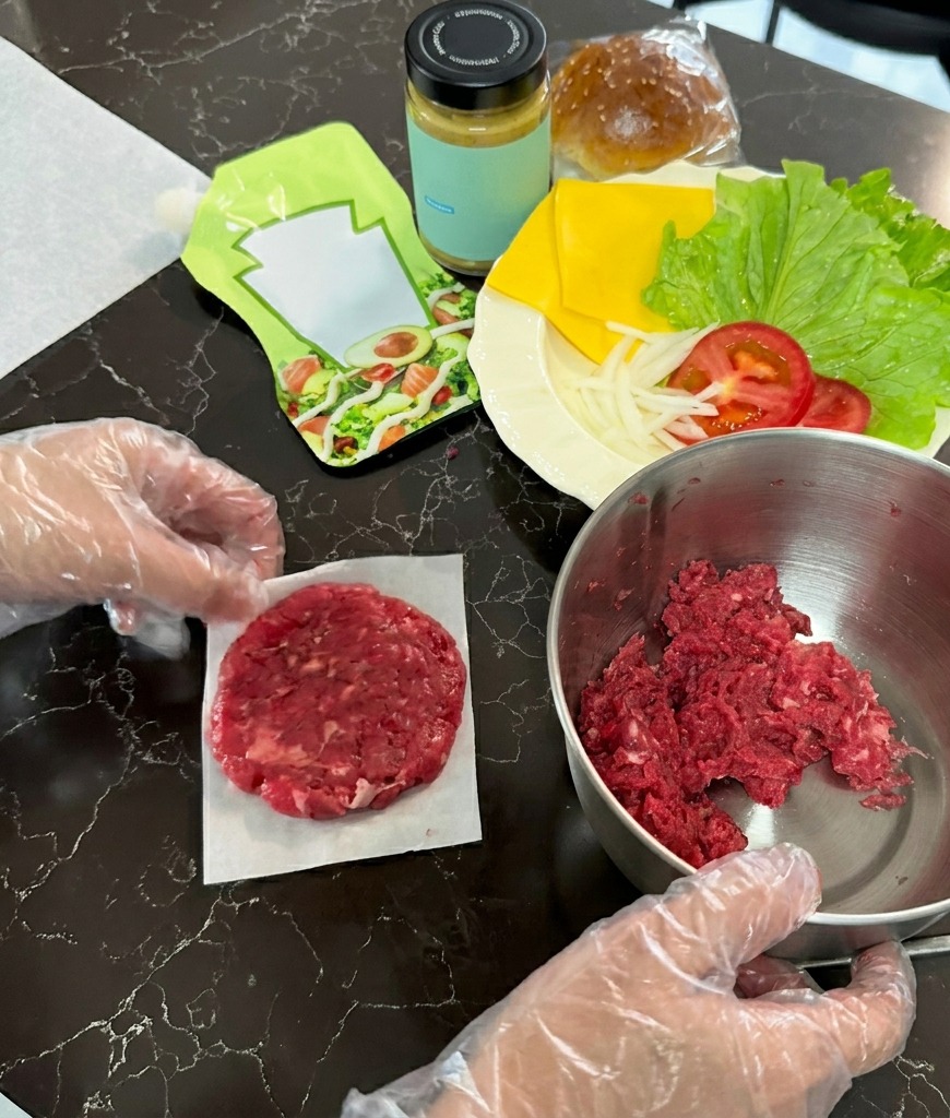 Ein rohes Rinder-Patty, das flach auf ein Stück weißes Backpapier gedrückt wurde, neben einer Schüssel mit Fleisch.