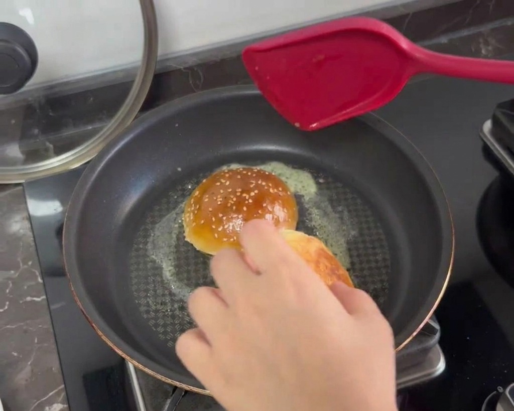 Halbierte Burgerbrötchen werden mit der Schnittseite nach unten in einer Pfanne mit schäumender Butter geröstet.