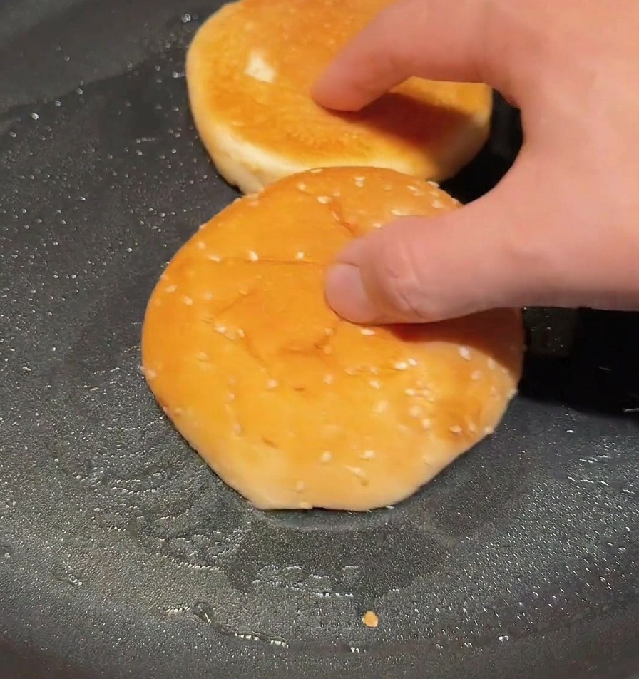 Halbierte Burgerbrötchen werden mit der Schnittfläche nach unten in einer trockenen Pfanne goldbraun geröstet.