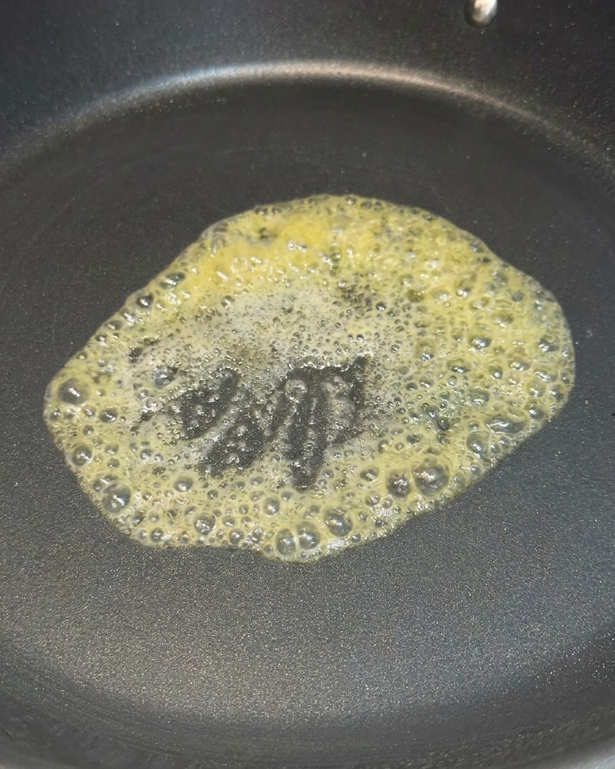 Ein Stück gelbe Butter schmilzt und schäumt in der Mitte einer schwarzen, beschichteten Pfanne.