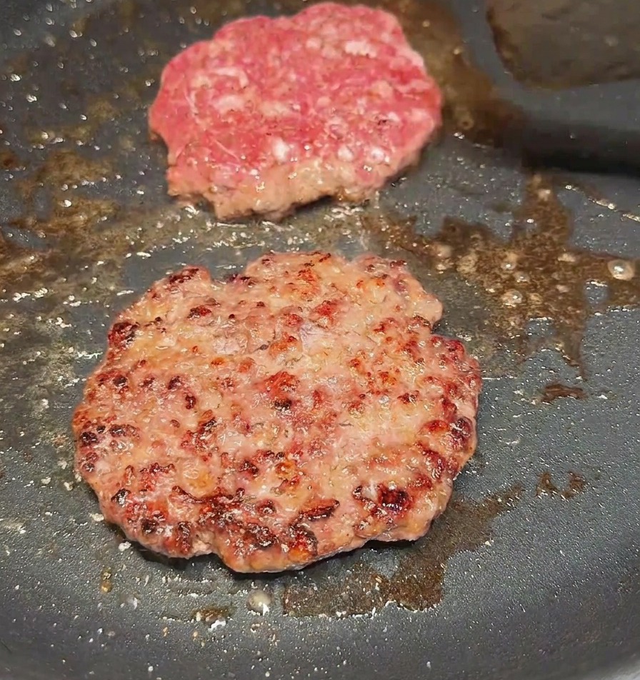 Ein Pfannenwender wendet ein Rinder-Patty und zeigt eine kräftig gebräunte, knusprige Kruste.