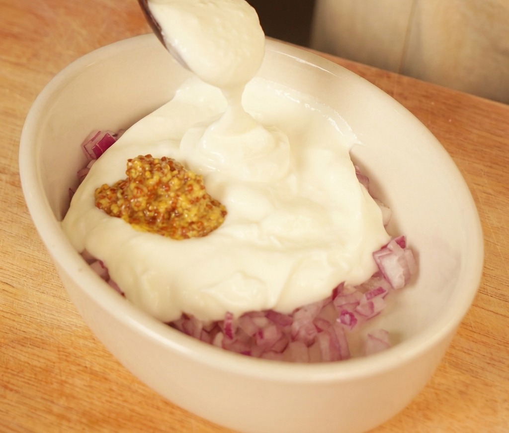 Ein Löffel cremiger Joghurt wird zu gehackten roten Zwiebeln und Senf in eine kleine Schale gegeben.