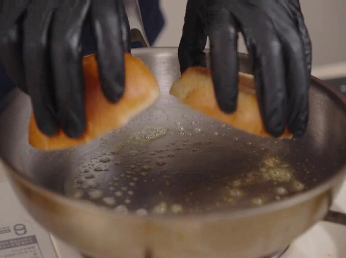 Zwei Hälften eines Brioche-Brötchens werden mit den Schnittflächen in eine Edelstahlpfanne mit schäumender Butter gelegt.