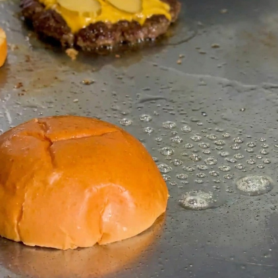 Die Oberseite eines Brioche-Brötchens wird auf der Grillplatte in Fett angeröstet.