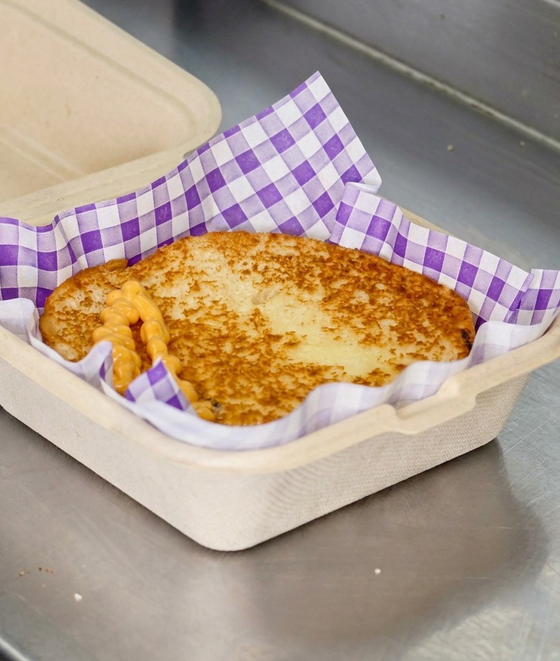 Orangefarbene Burgersauce, die in Zickzack-Linien auf einem getoasteten Brötchen verteilt wird.