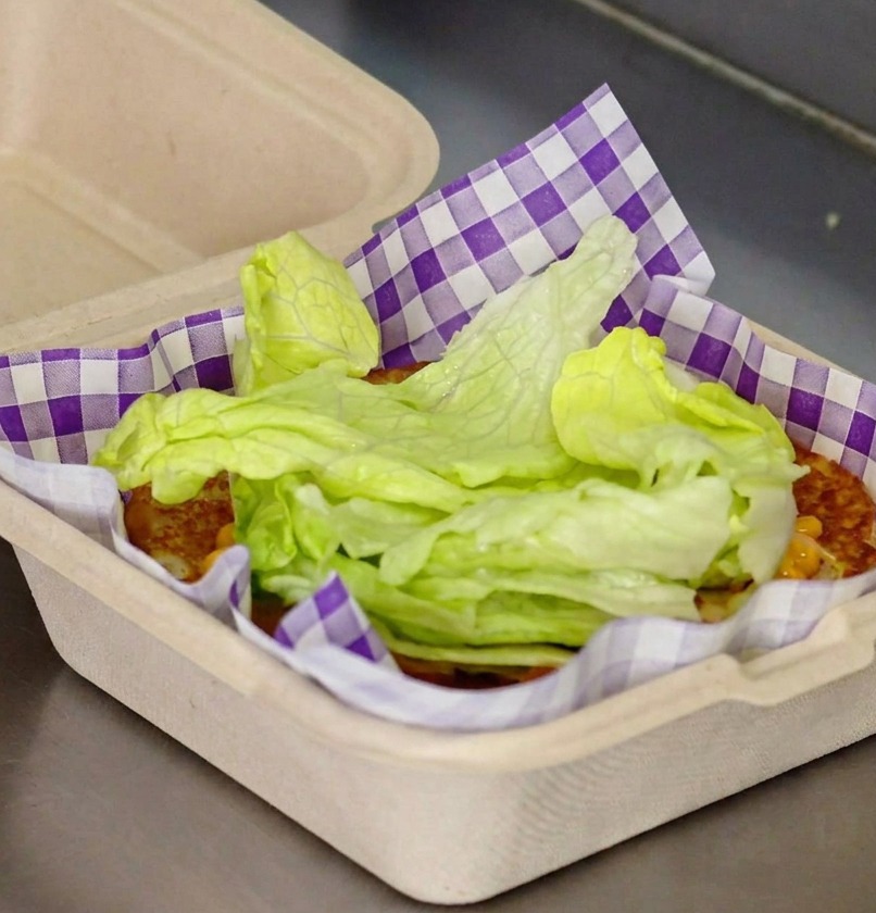 Frische grüne Salatblätter werden auf dem Brötchen mit Ketchup gestapelt.