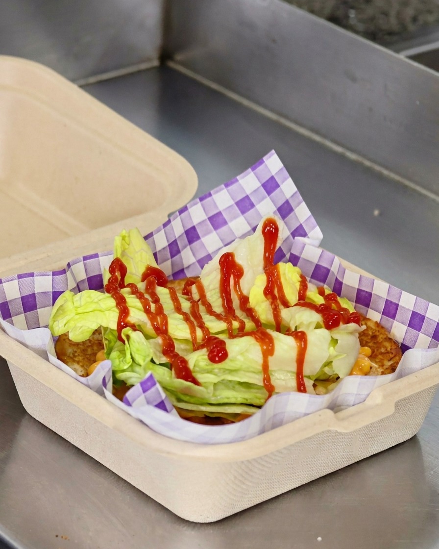 Rote Tomatenscheiben und ein Cheeseburger-Patty werden auf dem Salat im Brötchen platziert.