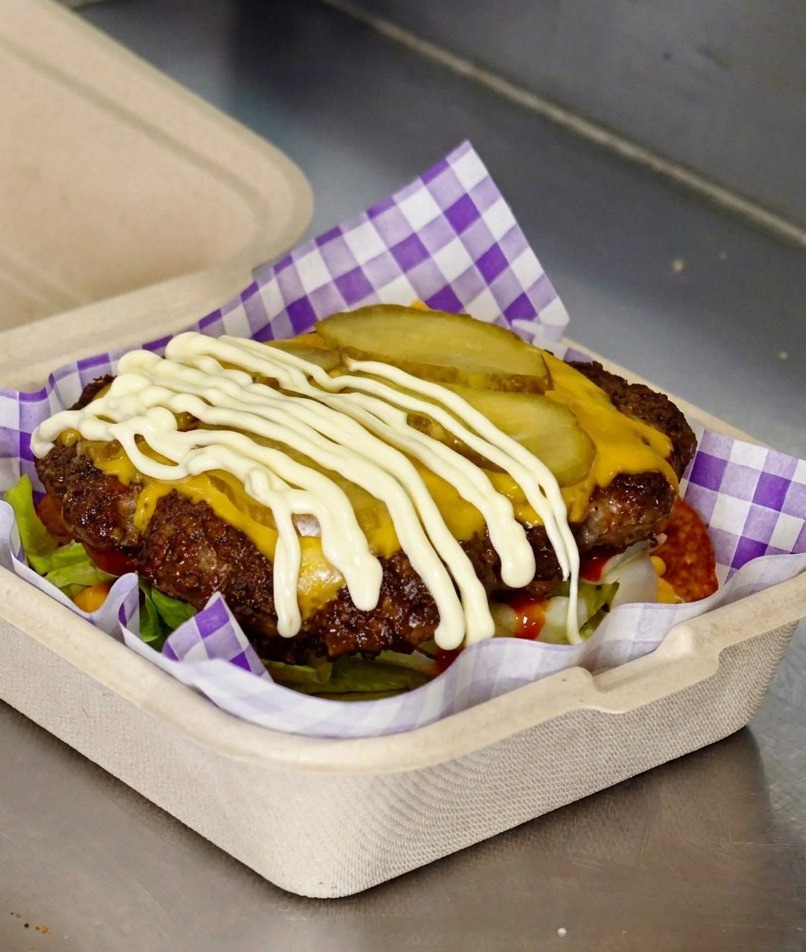 Weiße Mayonnaise wird über die Gurken auf dem Cheeseburger-Patty gegeben.