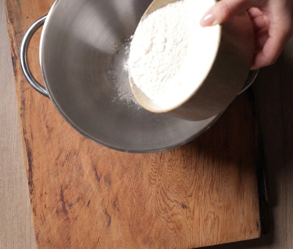 Feines weißes Mehl wird aus einer Schüssel in die Edelstahlschüssel einer Küchenmaschine gegossen.