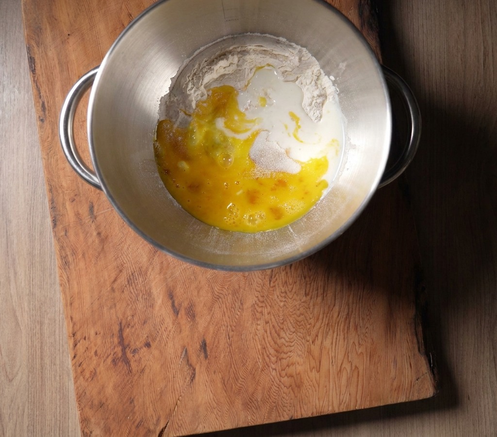 Frische Milch wird von oben in die Rührschüssel zur Mehl-Ei-Mischung gegossen.
