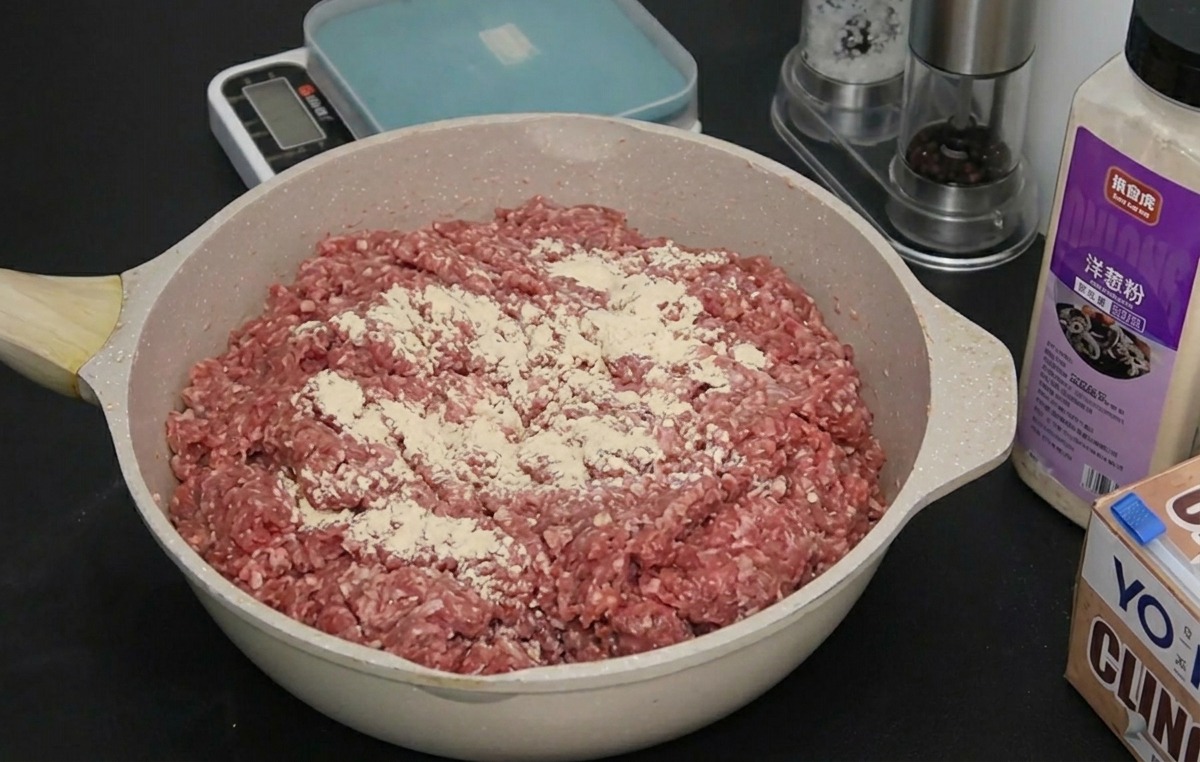 Rohes Rinderhackfleisch in einer Pfanne, bestreut mit einer feinen Schicht aus weißem Zwiebel- und Knoblauchpulver.