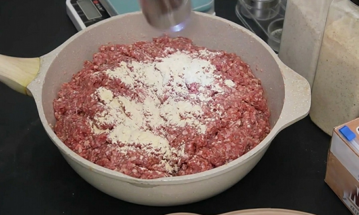 Eine elektrische Gewürzmühle aus Edelstahl mahlt schwarzen Pfeffer über das gewürzte rohe Fleisch in einer Pfanne.