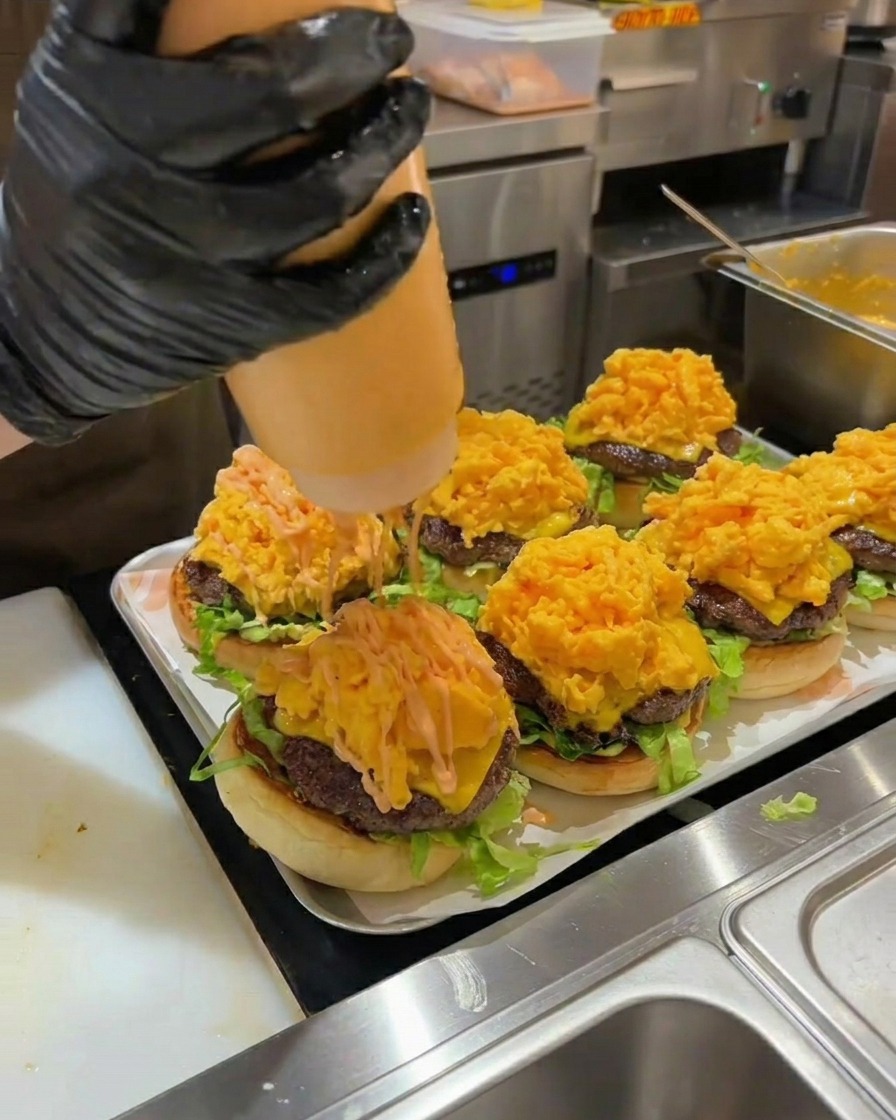 Orangefarbene Burgersauce wird über den hohen Berg Rührei auf dem fertigen Burger gegeben.