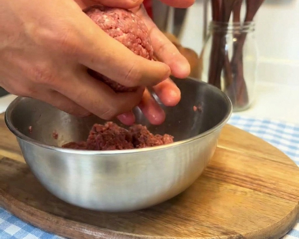 Hände werfen eine Kugel aus rohem Hackfleisch in die Handfläche, um die Textur vor dem Formen zu verdichten.