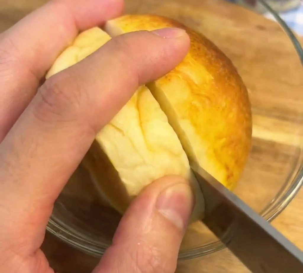 Ein Brotmesser schneidet ein perfekt geröstetes, goldbraunes Burger-Bun auf einem Holzbrett auf.
