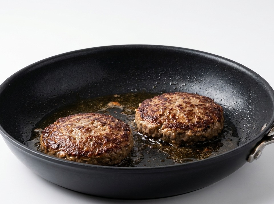 Zwei gewendete Rindfleisch-Patties in einer Pfanne, die eine knusprige, dunkelbraune Kruste aufweisen.