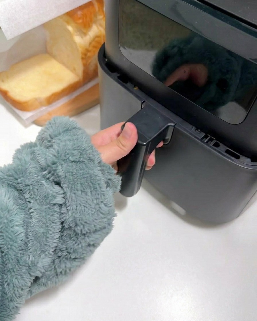 Eine Hand schließt das Fach einer schwarzen Heißluftfritteuse.