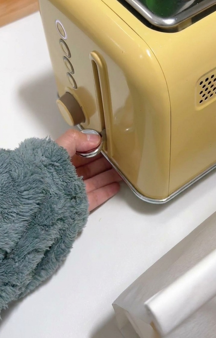 Eine Hand drückt den Hebel eines gelben Toasters nach unten, um das Brot zu bräunen.