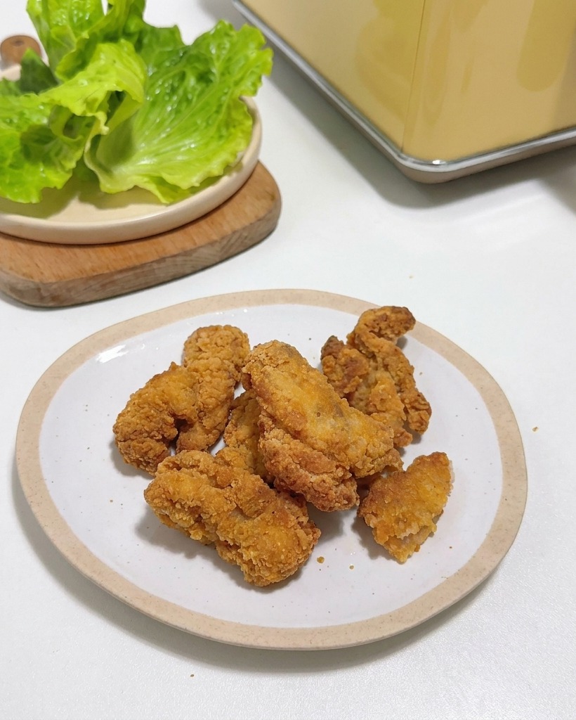 Knusprige Hähnchenteile auf einem kleinen weißen Teller neben frischen Salatblättern.