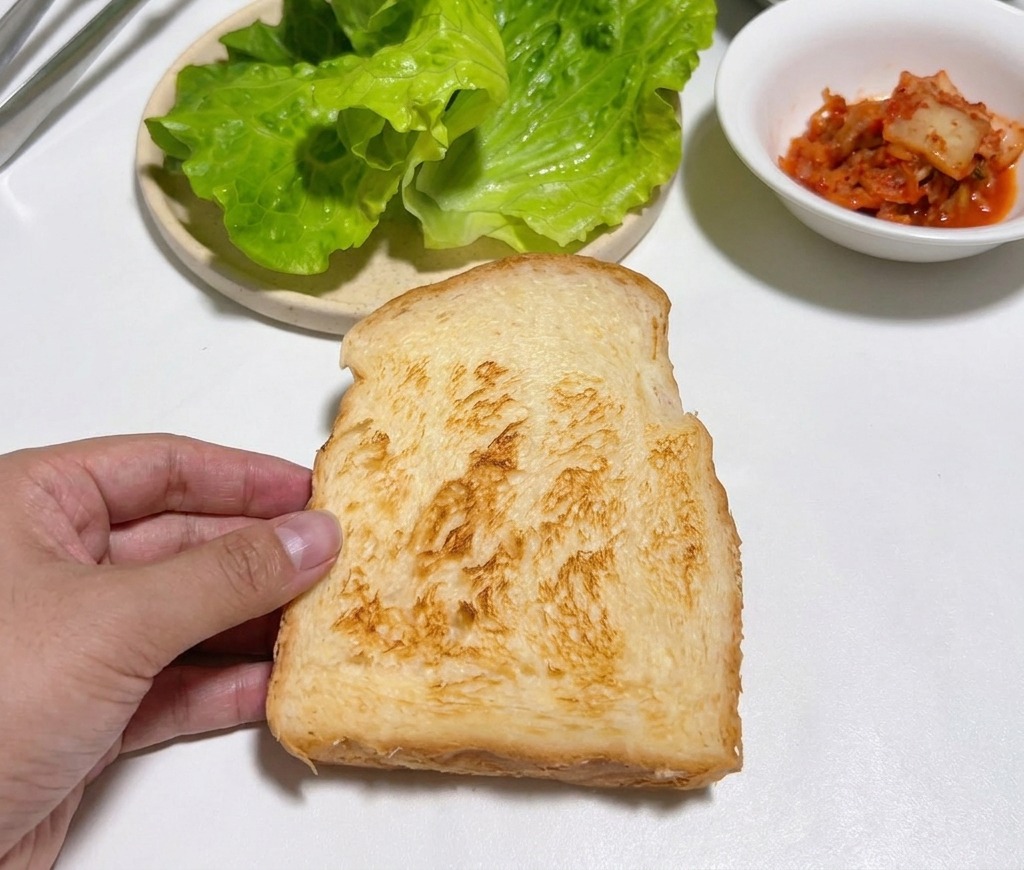 Eine Hand hält eine goldbraune Scheibe Toast über einen weißen Tisch.