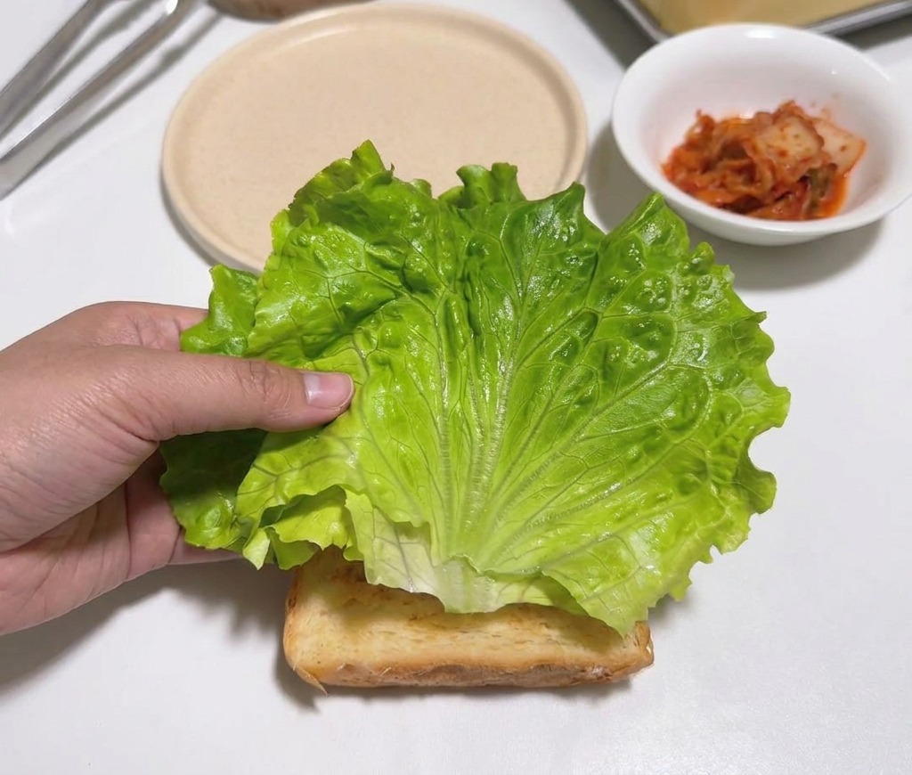 Eine Hand legt ein frisches grünes Salatblatt auf eine Toastscheibe.