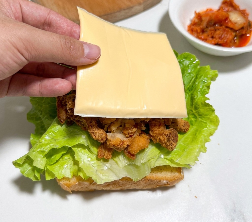 Eine Hand legt eine Scheibe gelben Käse auf die Hähnchenteile im Sandwich.