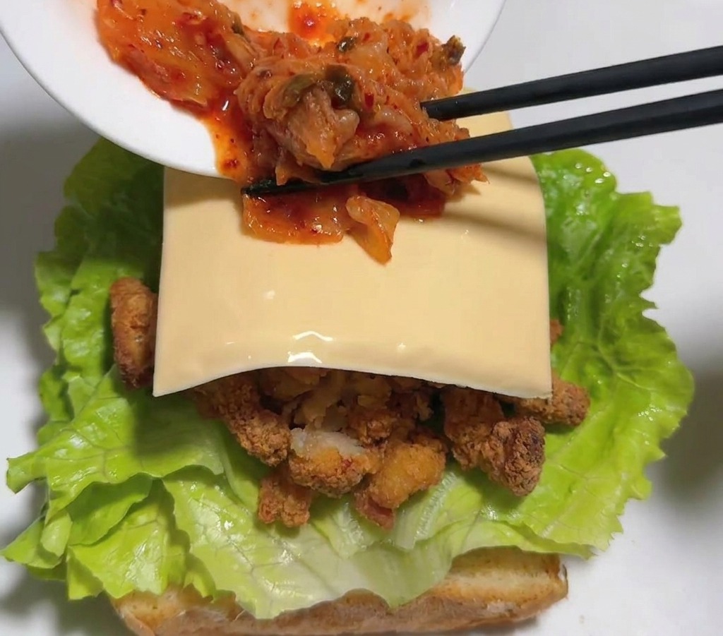 Schwarze Stäbchen legen rotes Kimchi auf die Käsescheibe im Sandwich.
