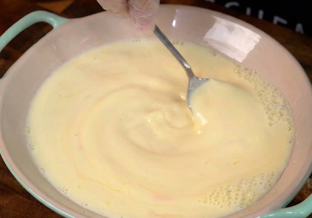 Milch und Eier mit sichtbaren Honigschlieren werden in einer hellrosa Keramikschüssel umgerührt.