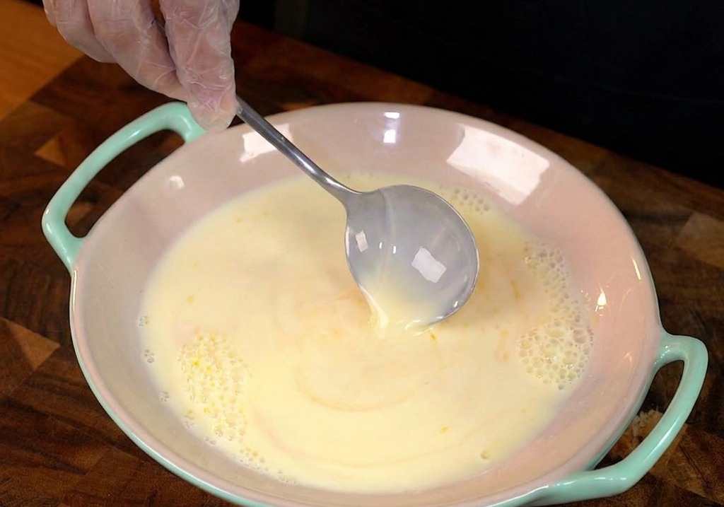 Eine dicke Scheibe Weißbrot wird in einen flachen Teller mit gelber Eiermilch getaucht.