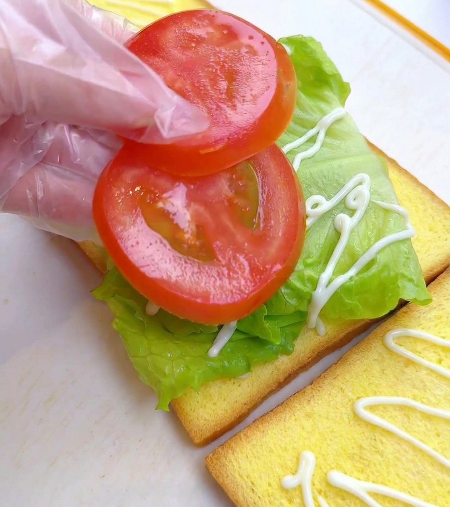 Zwei runde Tomatenscheiben werden auf das Salatbett des Sandwiches gelegt.