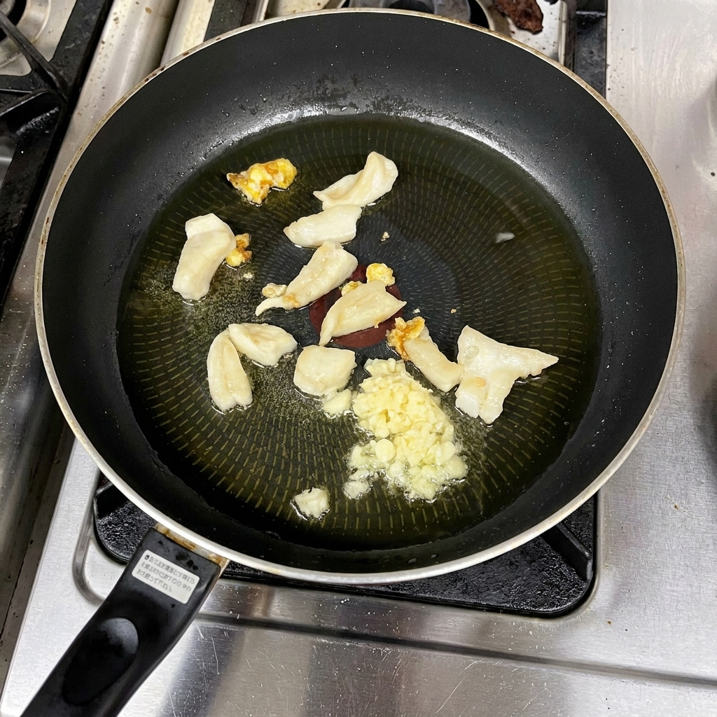 Gehackter Knoblauch und Fettstücke braten in einer Pfanne in flüssigem, klarem Öl.