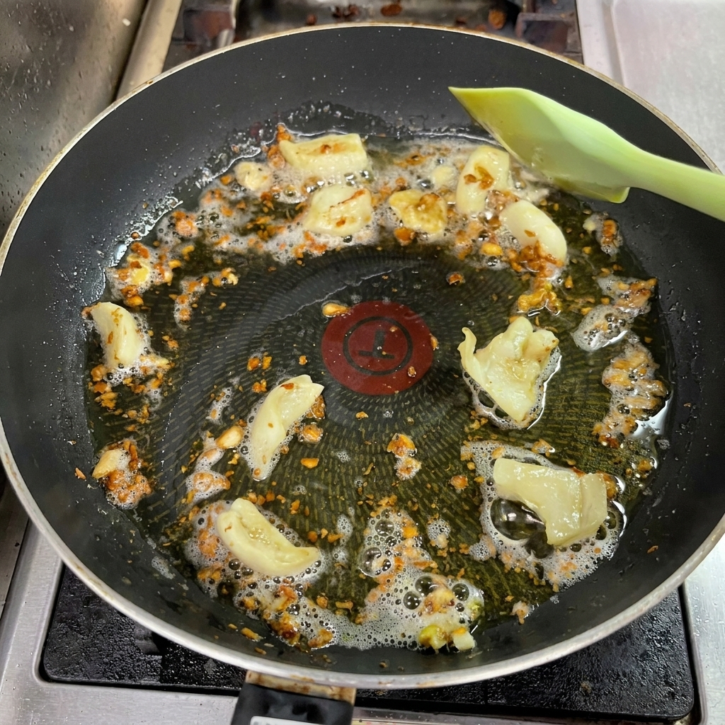 Gehackter Knoblauch brät in Öl in einer Pfanne, wird tief goldbraun und wird mit einem Pfannenwender gerührt.