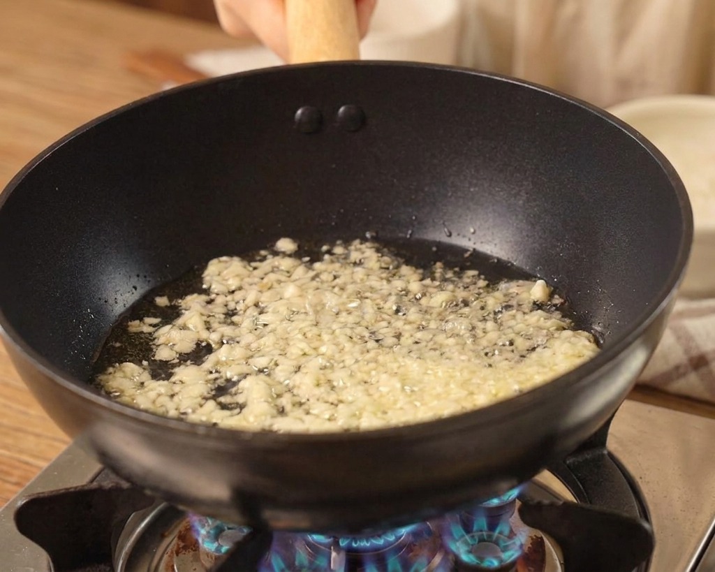 Fein gehackter Knoblauch brutzelt in Öl in einem schwarzen Wok.