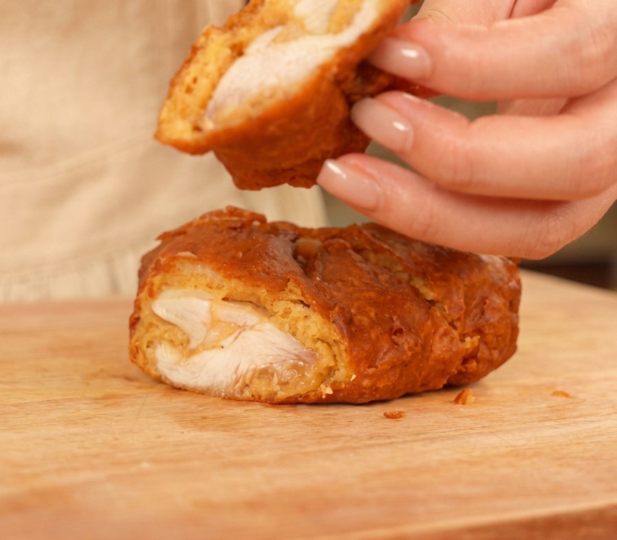 Aufgeschnittenes Fried Chicken auf einem Holzbrett mit saftigem Fleisch und dicker goldener Kruste.