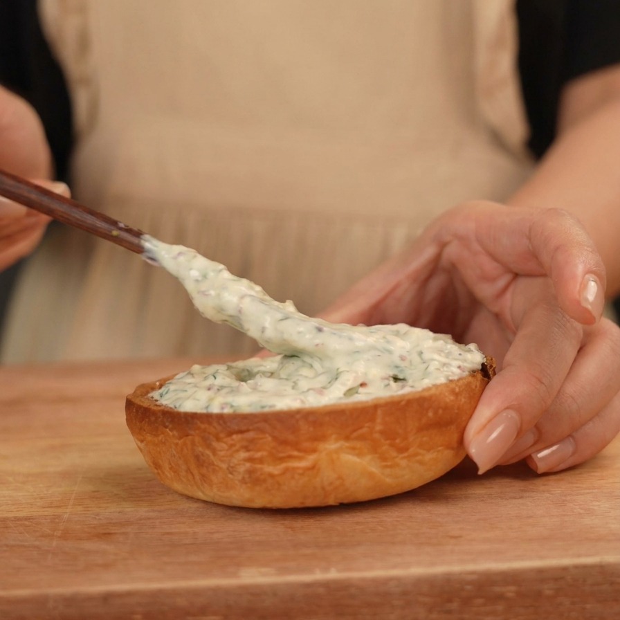Eine weiße Sauce wird mit einem Spatel auf die untere Hälfte eines getoasteten Brioche-Buns gestrichen.