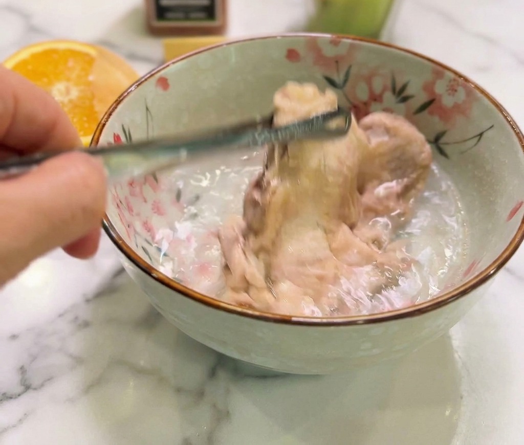 Gekochtes Hähnchen wird in eine Keramikschüssel mit klarem, kaltem Wasser getaucht, um den Garprozess zu stoppen.