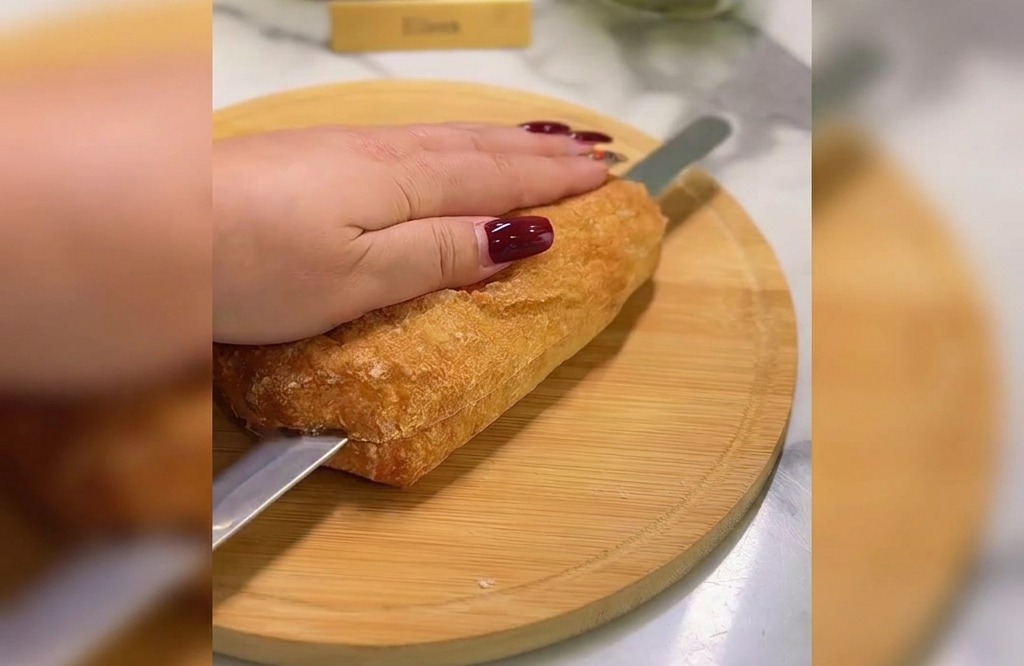 Eine Hand hält ein goldbraunes Ciabatta-Brot fest, während ein gezacktes Brotmesser es auf einem runden Holzbrett horizontal durchschneidet.