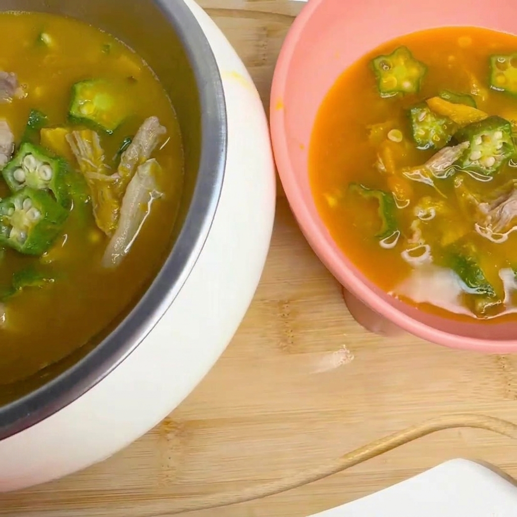 Eine Schöpfkelle rührt sanft eine leicht köchelnde Suppe mit Okra und Entenstücken in einem Topf um.