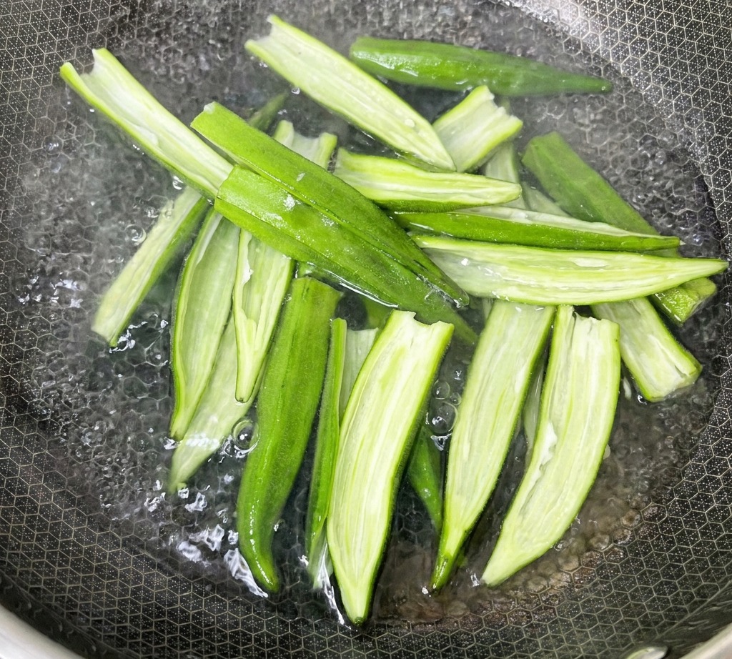 Aufgeschnittene Okraschalen kochen in einem Topf mit Wasser auf dem Herd.
