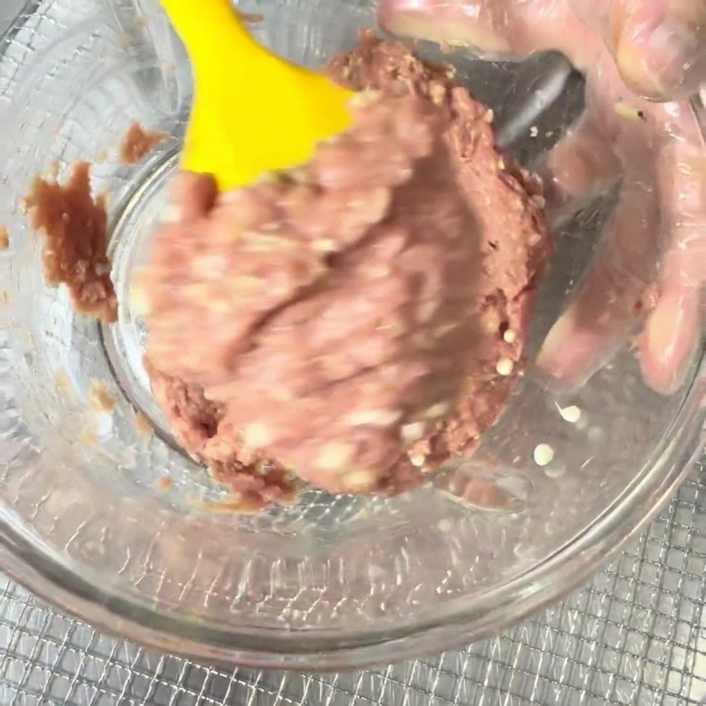 Entenhackfleisch und Okrasamen, die in einer Schüssel mit einem gelben Silikonspatel vermengt werden.