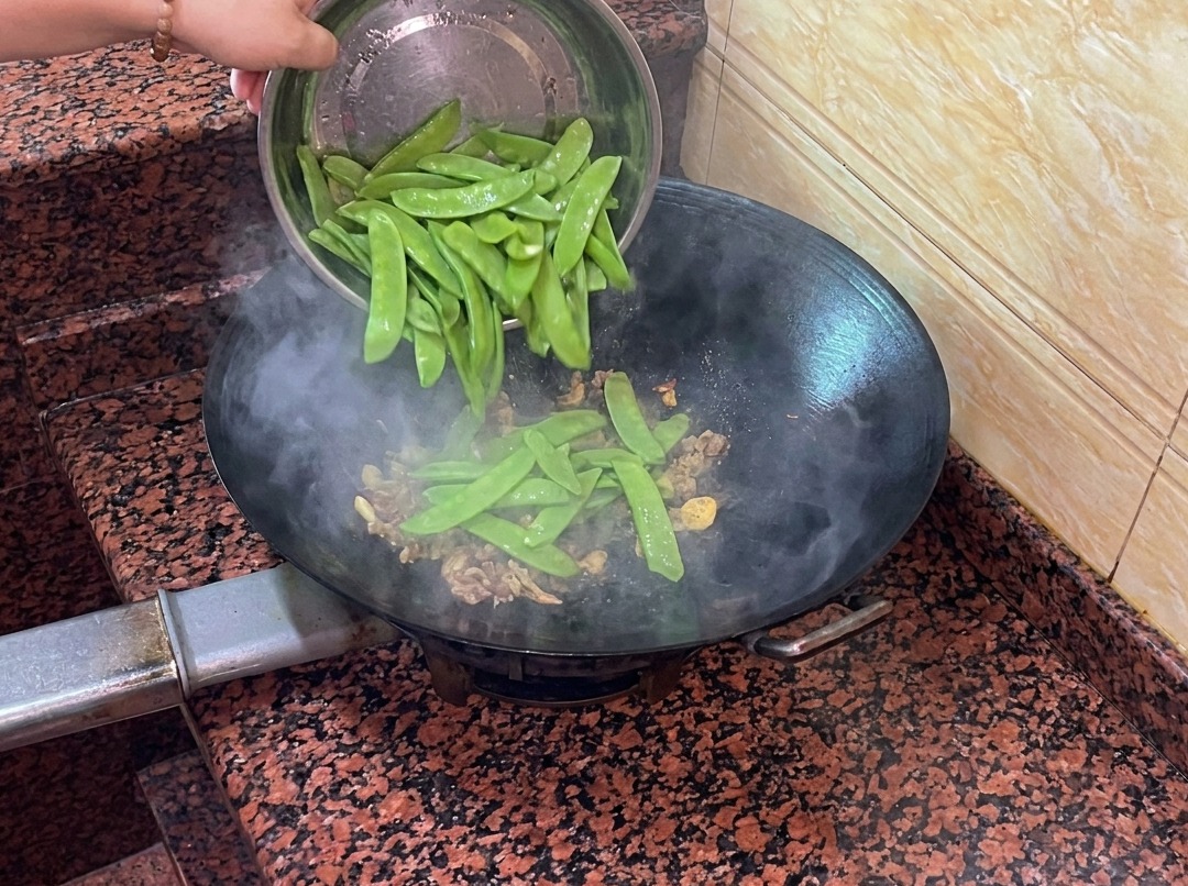 Frische Kaiserschoten werden in den Wok zu Wurst und Aromaten gegeben.