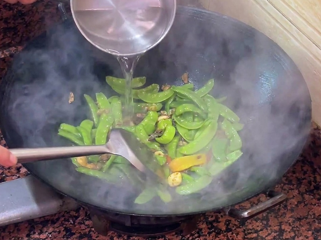 Warmes Wasser wird in den Wok zu den Kaiserschoten und der Wurst gegeben.