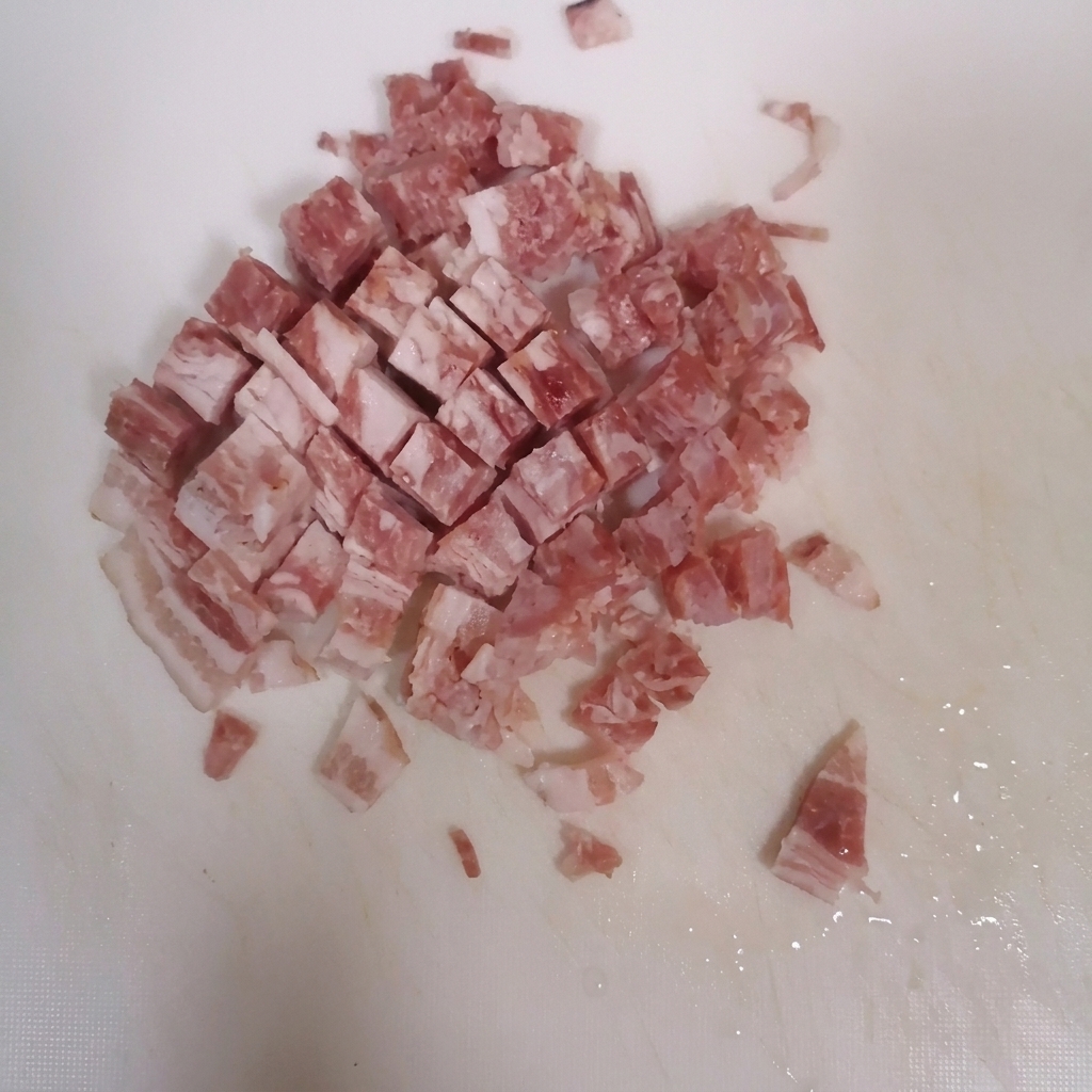 Speckstreifen werden auf einem sauberen weißen Schneidebrett in kleine Würfel geschnitten.