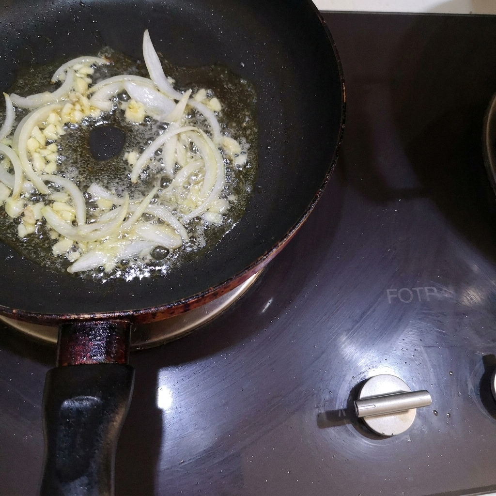 Gewürfelte Zwiebeln und gehackter Knoblauch werden in der geschmolzenen Butter in einer Pfanne umgerührt.