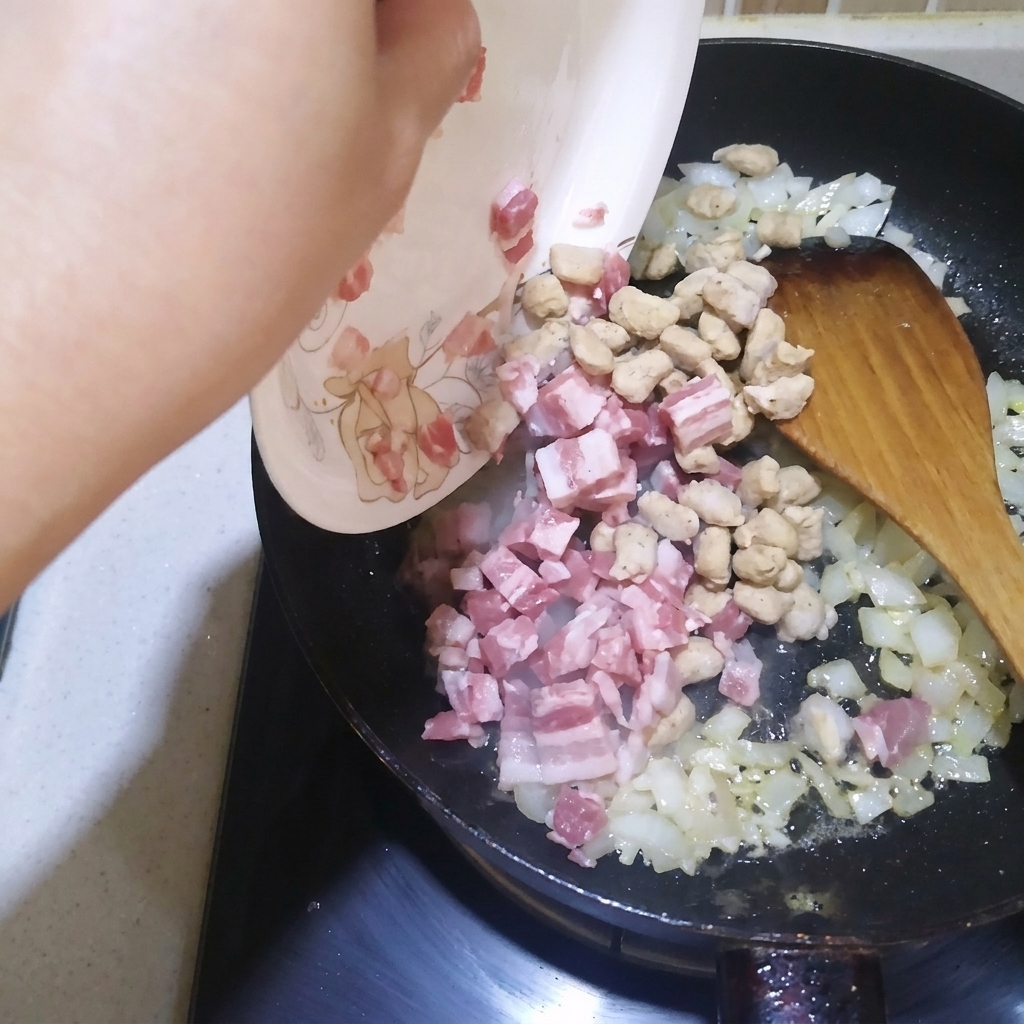 Gewürfelter Speck und Rindfleischwürfel werden mit Zwiebeln und Knoblauch in der Pfanne angebraten.