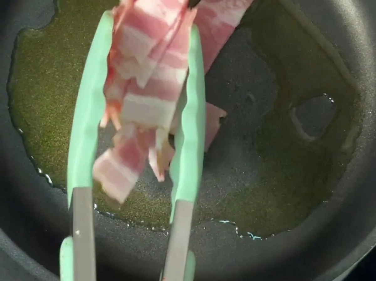 Krosser Speck brät in Olivenöl in einer beschichteten Pfanne.
