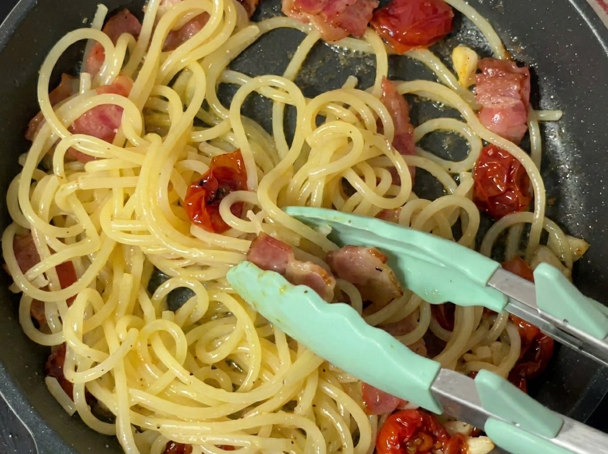 Schwarzer Pfeffer wird frisch über die gekochte Pasta in der Pfanne gemahlen.